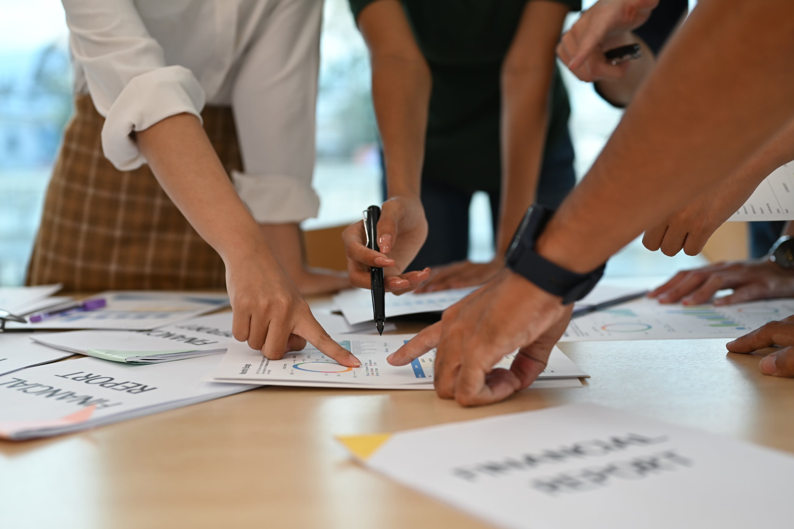 A group of people gathered around a table with papers and financial documents spread out, collaboratively discussing or working on a project together.